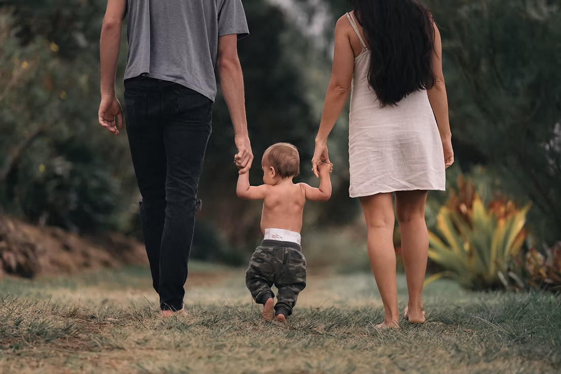Parents walking outdoors holding their toddler's hands after a surrogacy journey